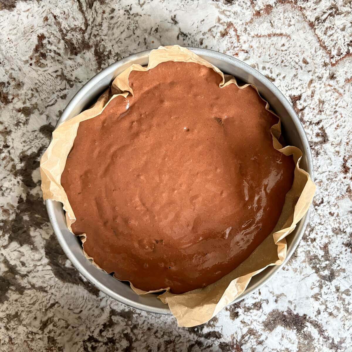 Cake batter in a baking pan lined with parchment paper.