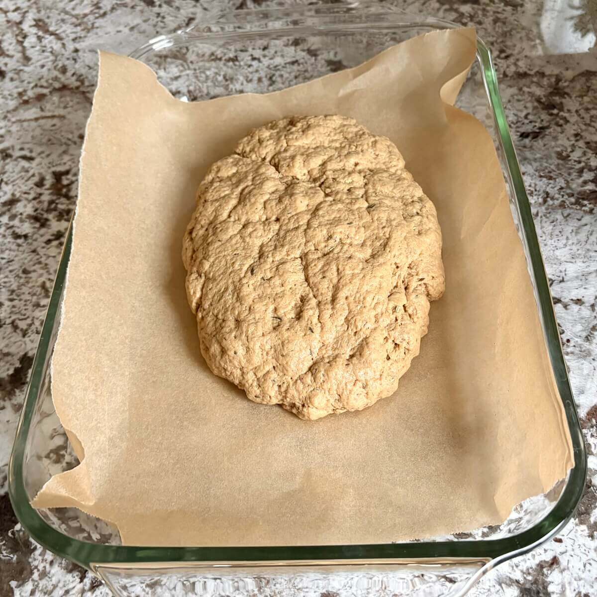 Raw dough for a vegan roast in a glass baking dish lined with parchment paper.