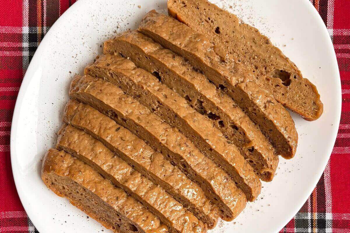 A sliced vegan holiday roast on a plate sprinkled with pepper.