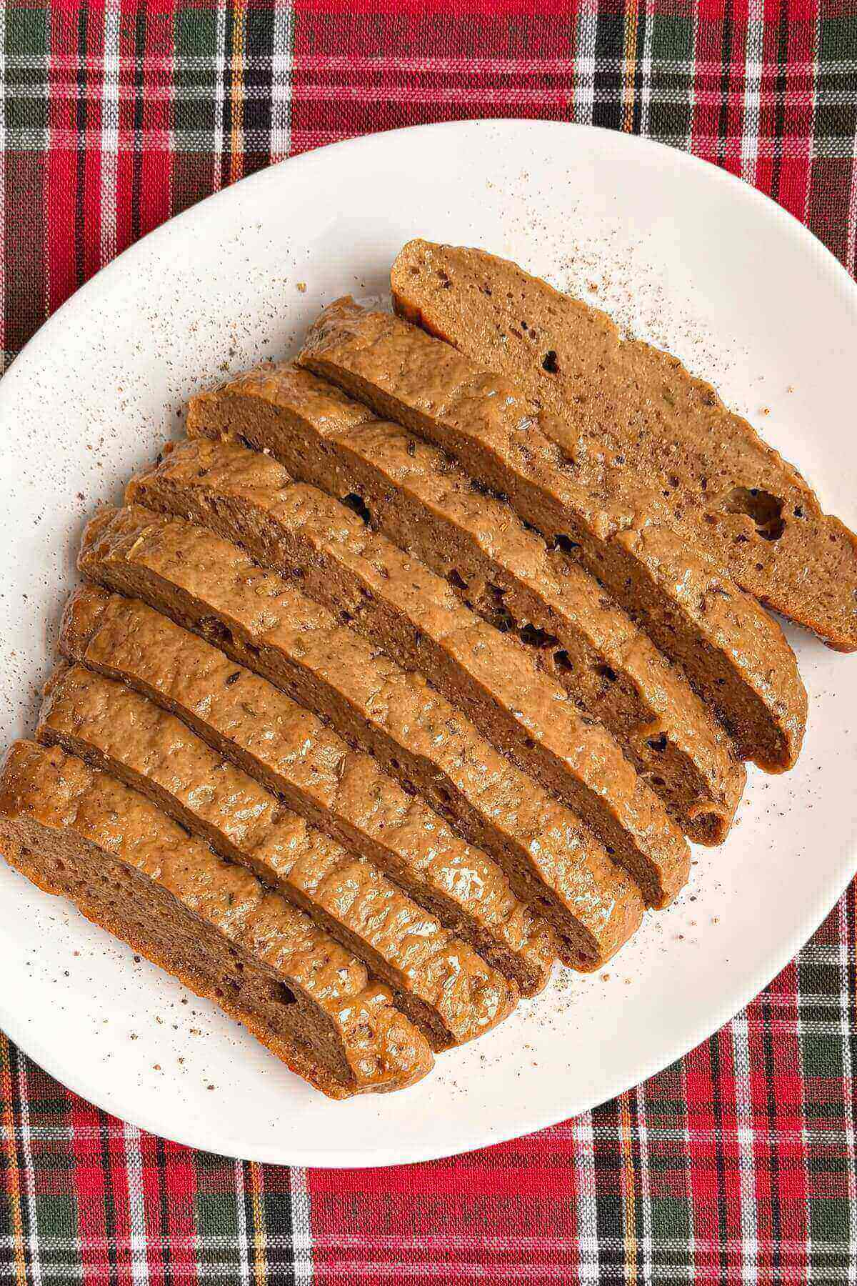 Slices of vegan roast on a plate on a red and green plaid placemat.