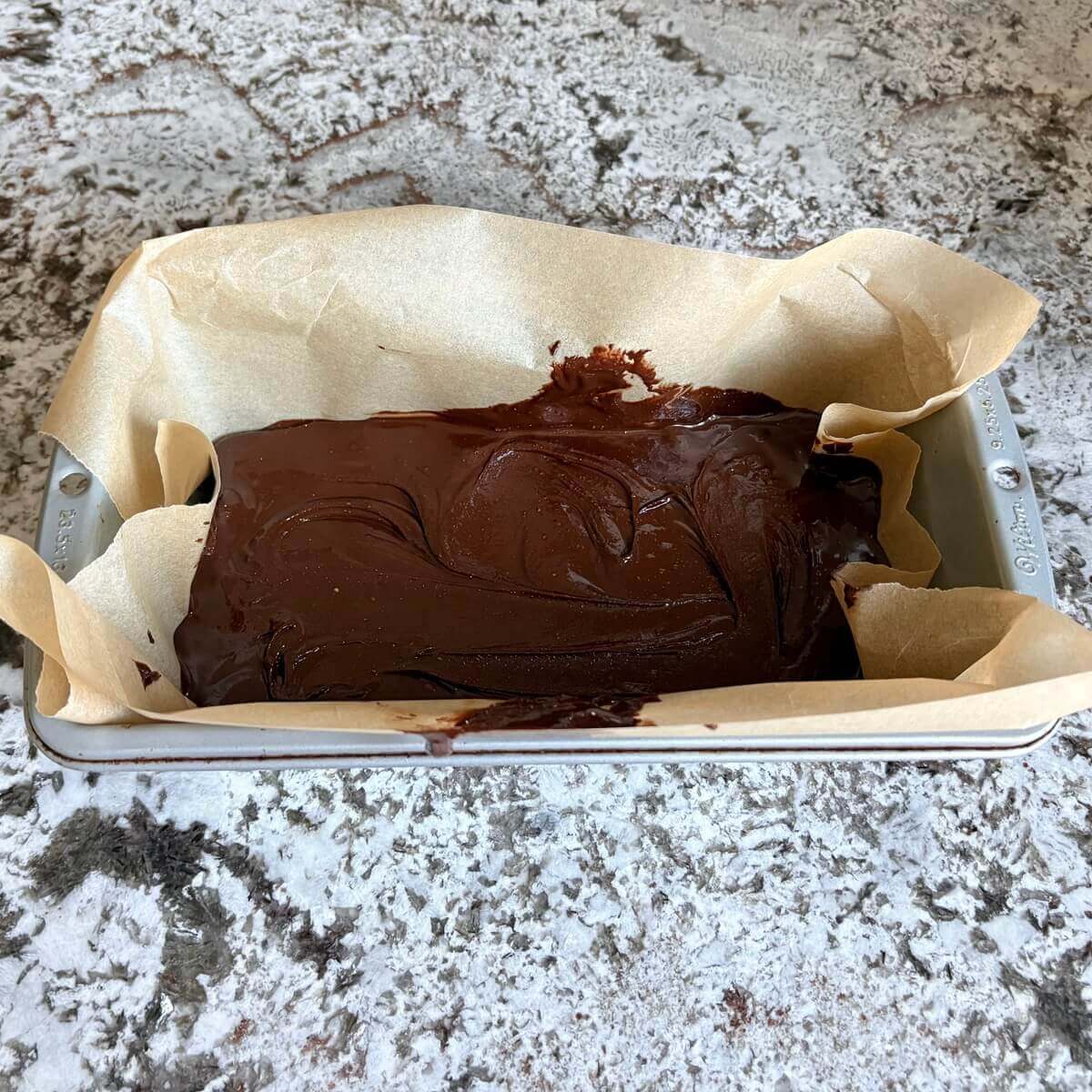Fudge batter made with almond butter in a loaf pan lined with parchment paper.
