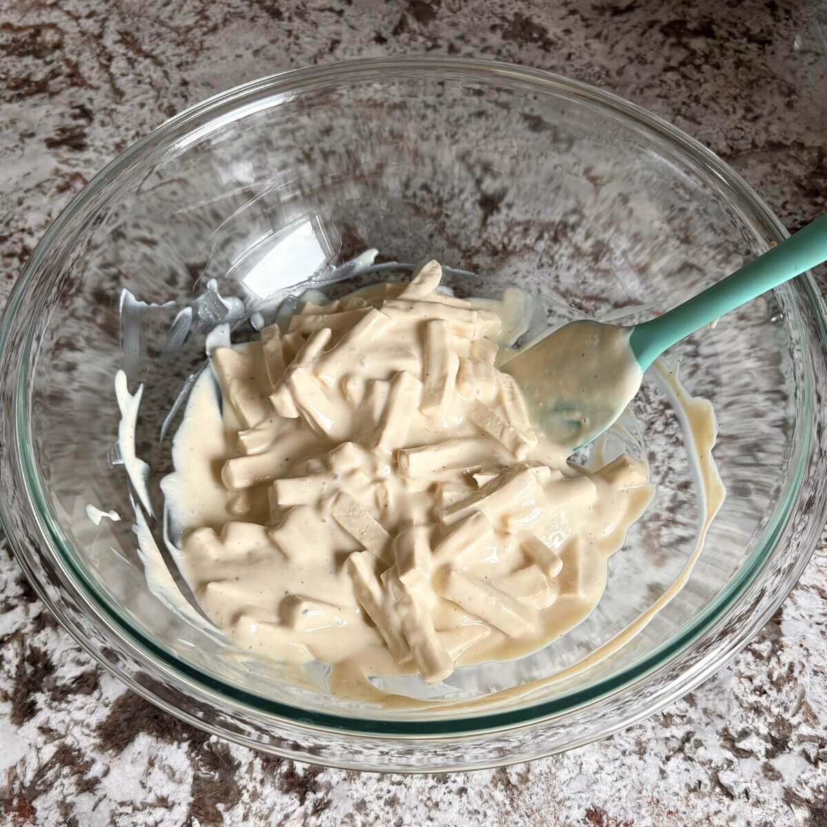 Tofu pieces in a creamy sauce in a glass mixing bowl.