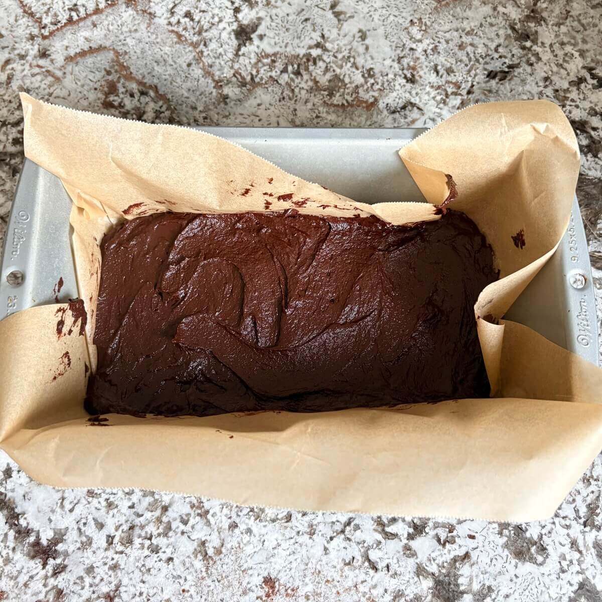 Raw fudge in a loaf pan lined with parchment paper.
