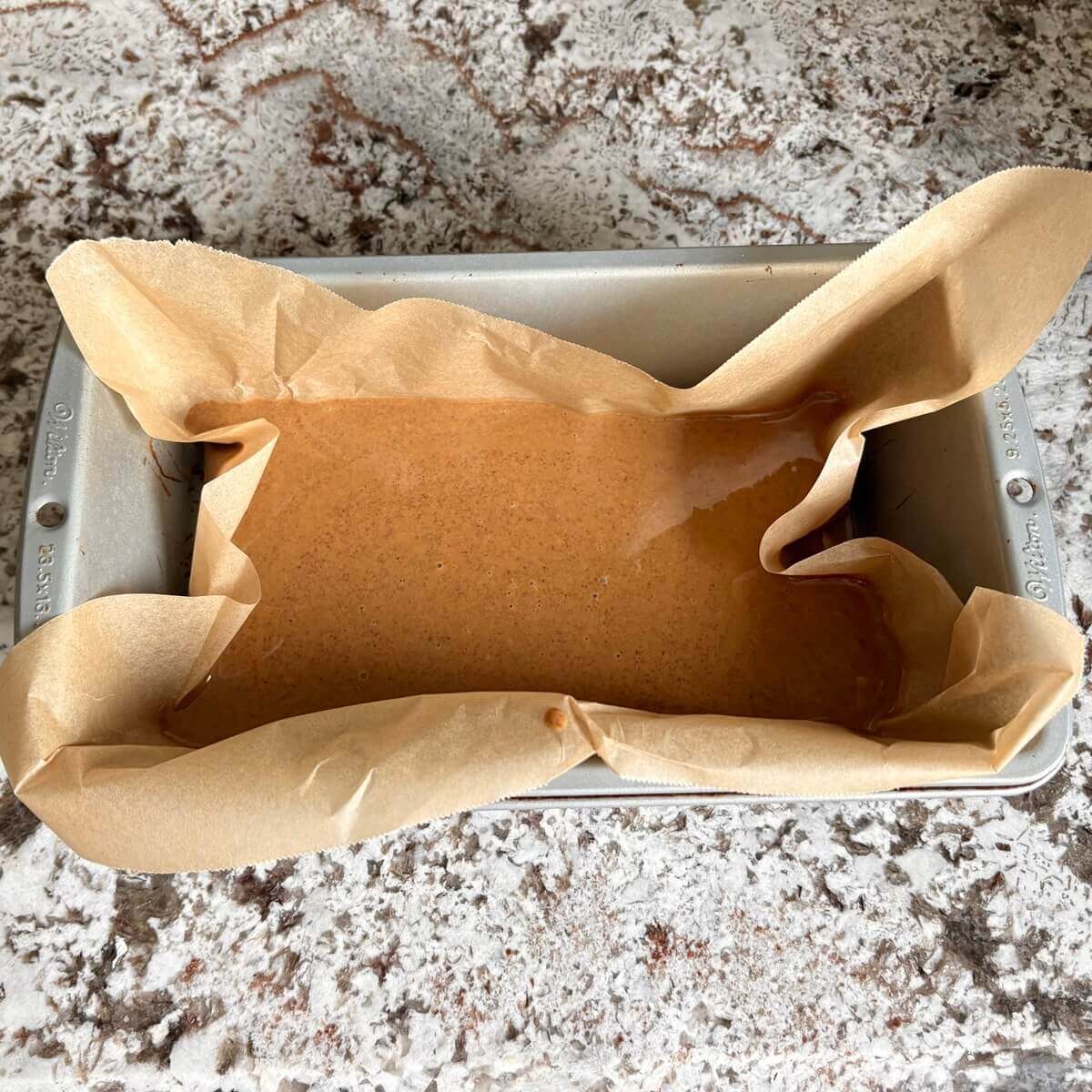 Gingerbread fudge batter in a loaf pan lined with parchment paper.