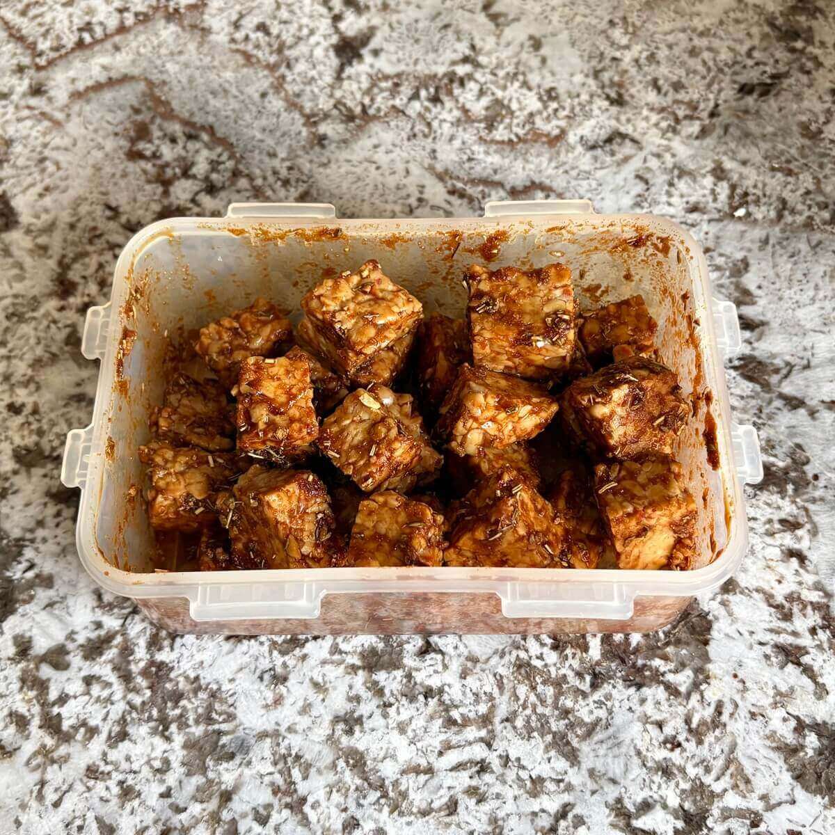 Raw tempeh cubes marinating in a plastic container.