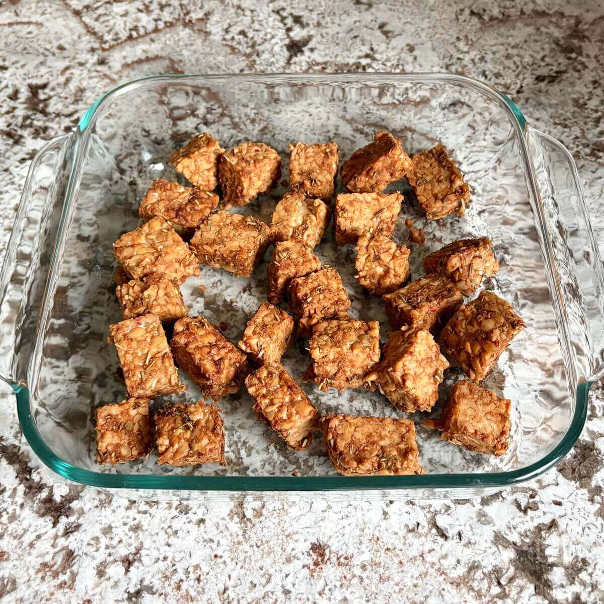 Pieces of marinated tempeh in a glass baking dish.