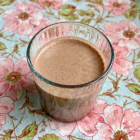 A creamy hemp heart smoothie in a glass on a floral placemat.