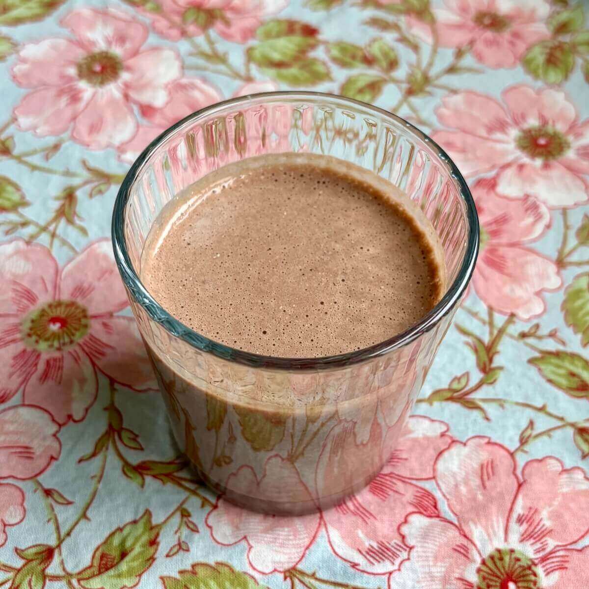 A creamy hemp heart smoothie in a glass on a floral placemat.