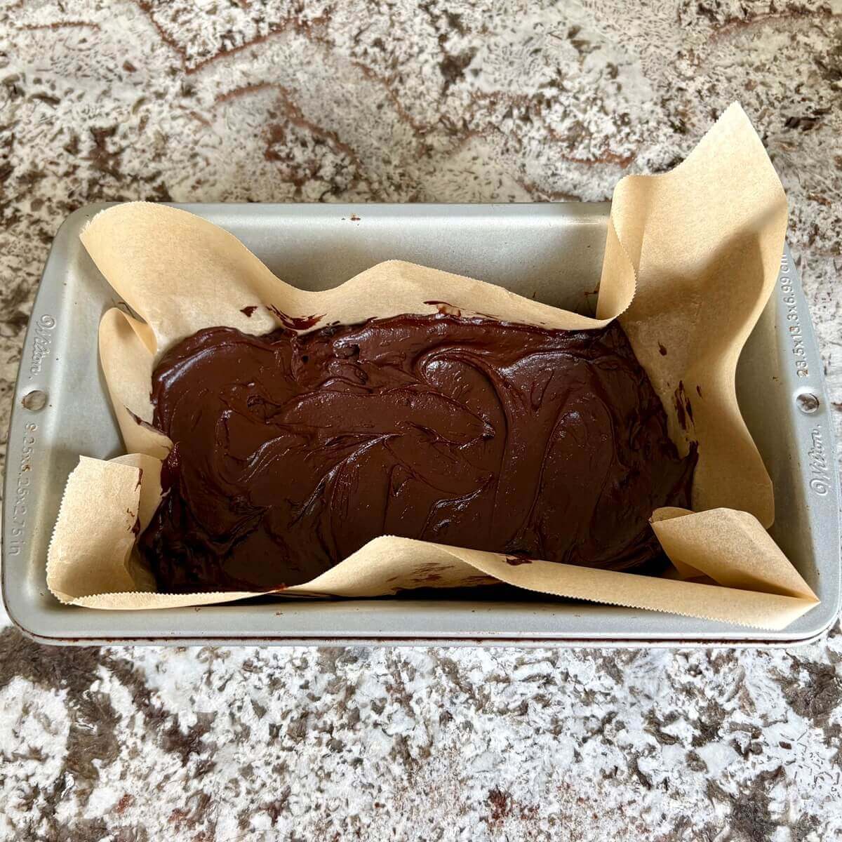 Raw fudge made with avocado in a loaf pan lined with parchment paper.