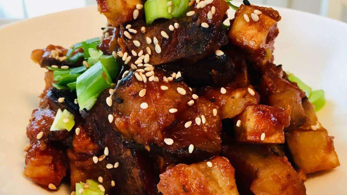 Vegan sweet and sour tofu garnished with sesame seeds and chopped green onions.