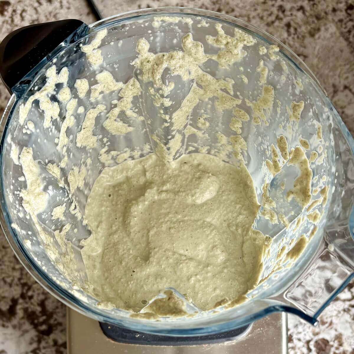 Blended pumpkin seeds and other ingredients for vegan cheese in a blender.