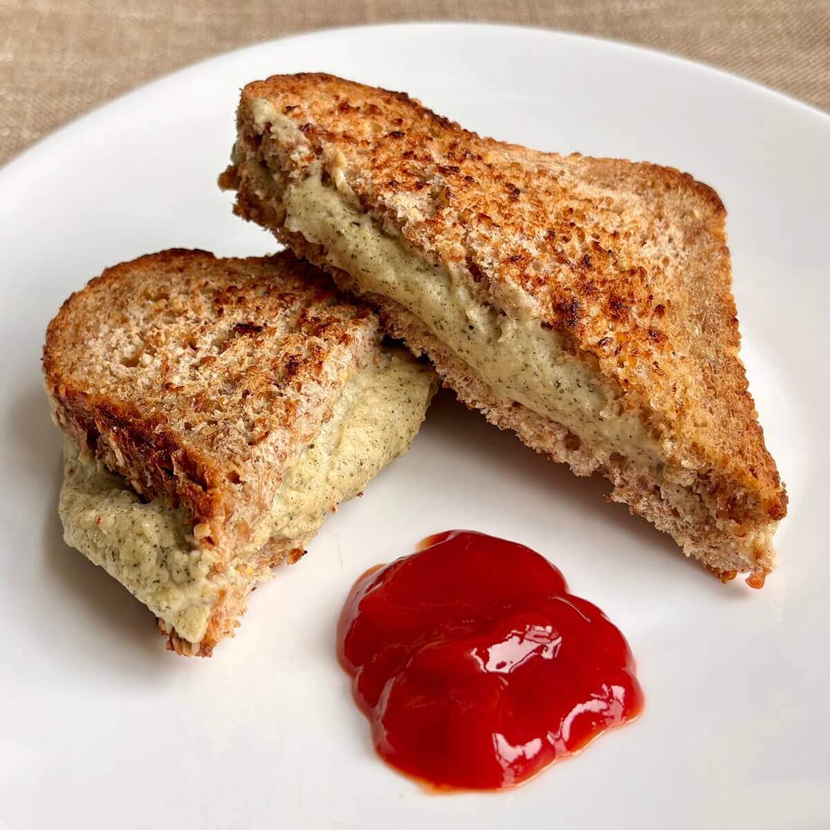 A sandwich filled with hemp cheese next to a blob of ketchup on a plate.
