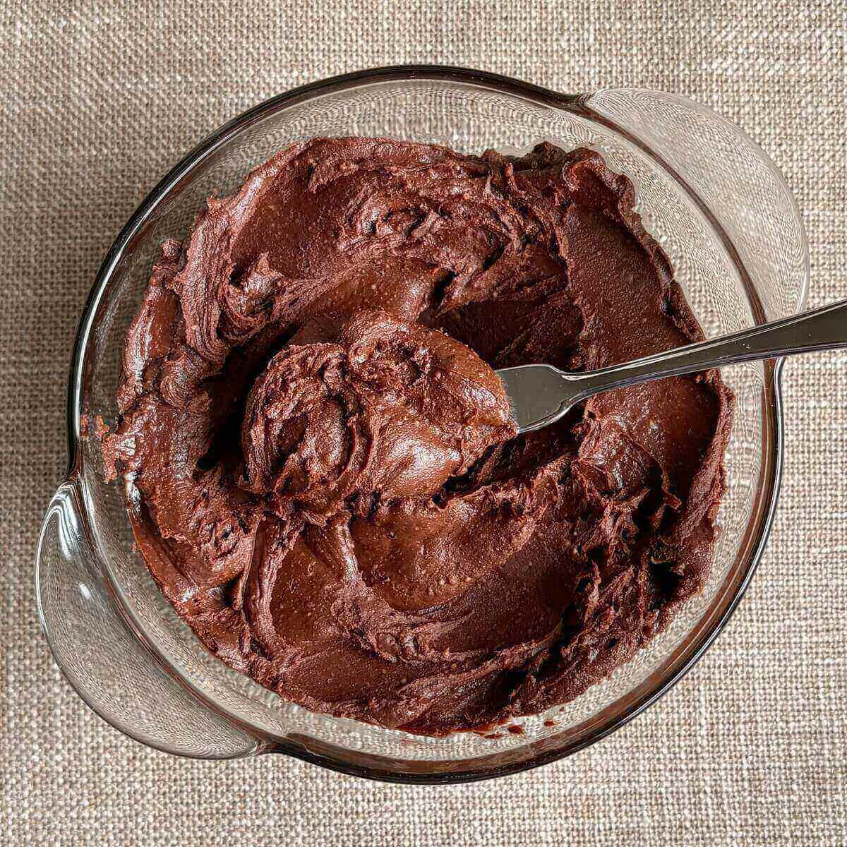 Low-sugar chocolate frosting in a glass bowl with a knife.