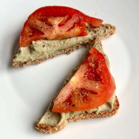 Toast with pumpkin seed cheese and tomato slices on a white plate.
