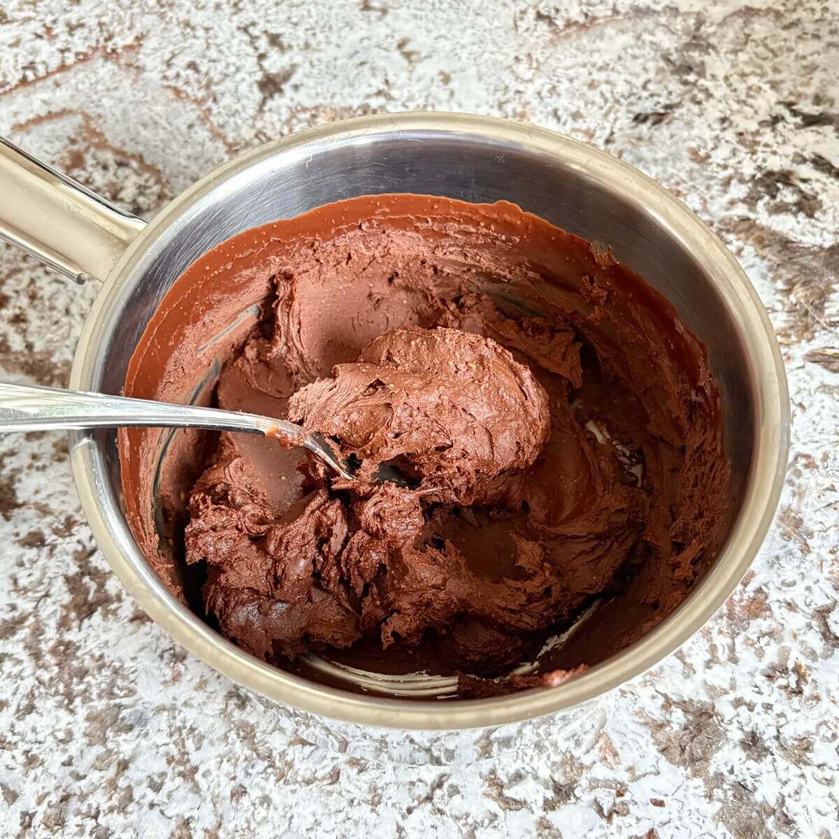 Thick frosting in a steel pot with a spoon.