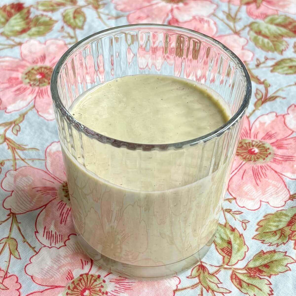An avocado oatmeal smoothie in a glass on a floral placemat.