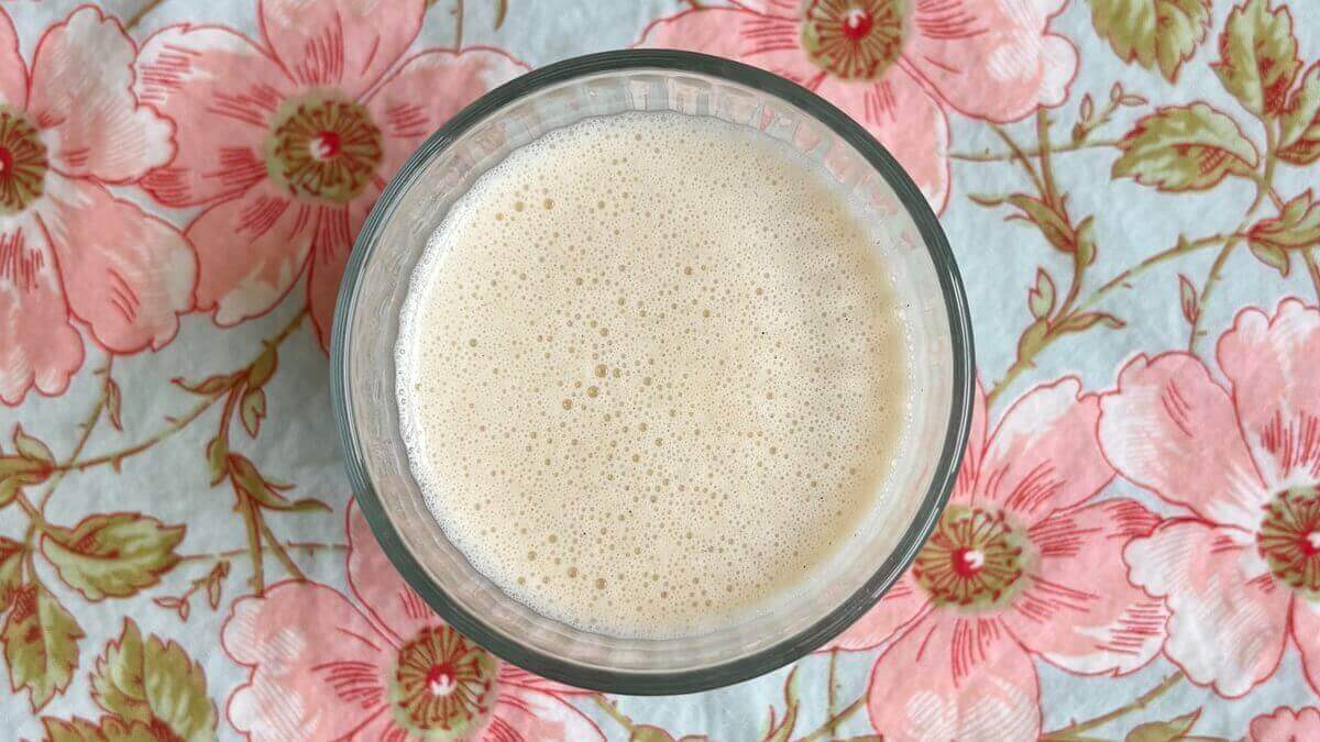 A banana shake made without yogurt in a glass on a floral placemat.