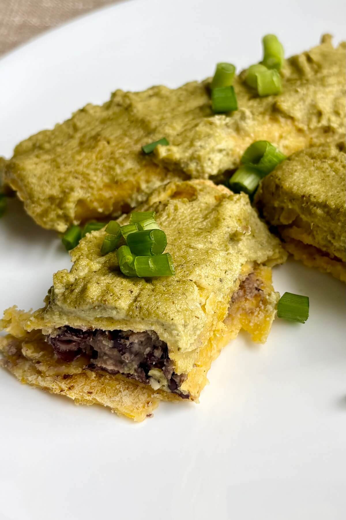 Vegan enchiladas garnished with green onions on a white plate.