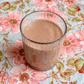 A cashew butter smoothie in a glass on a floral placemat.