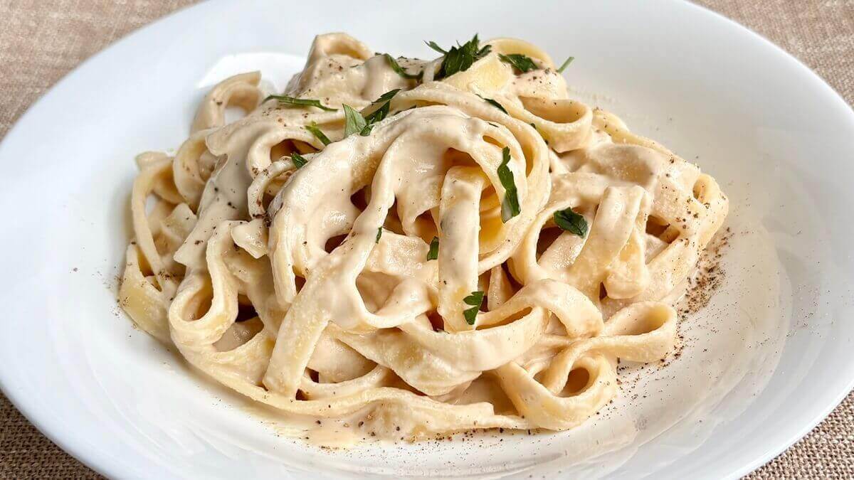 Fettucine noodles with a creamy sauce in a white bowl.
