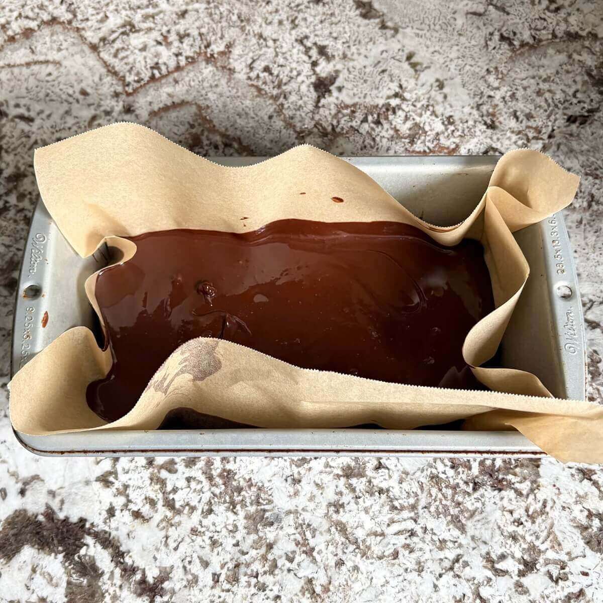 Fudge batter in a loaf pan lined with parchment paper.