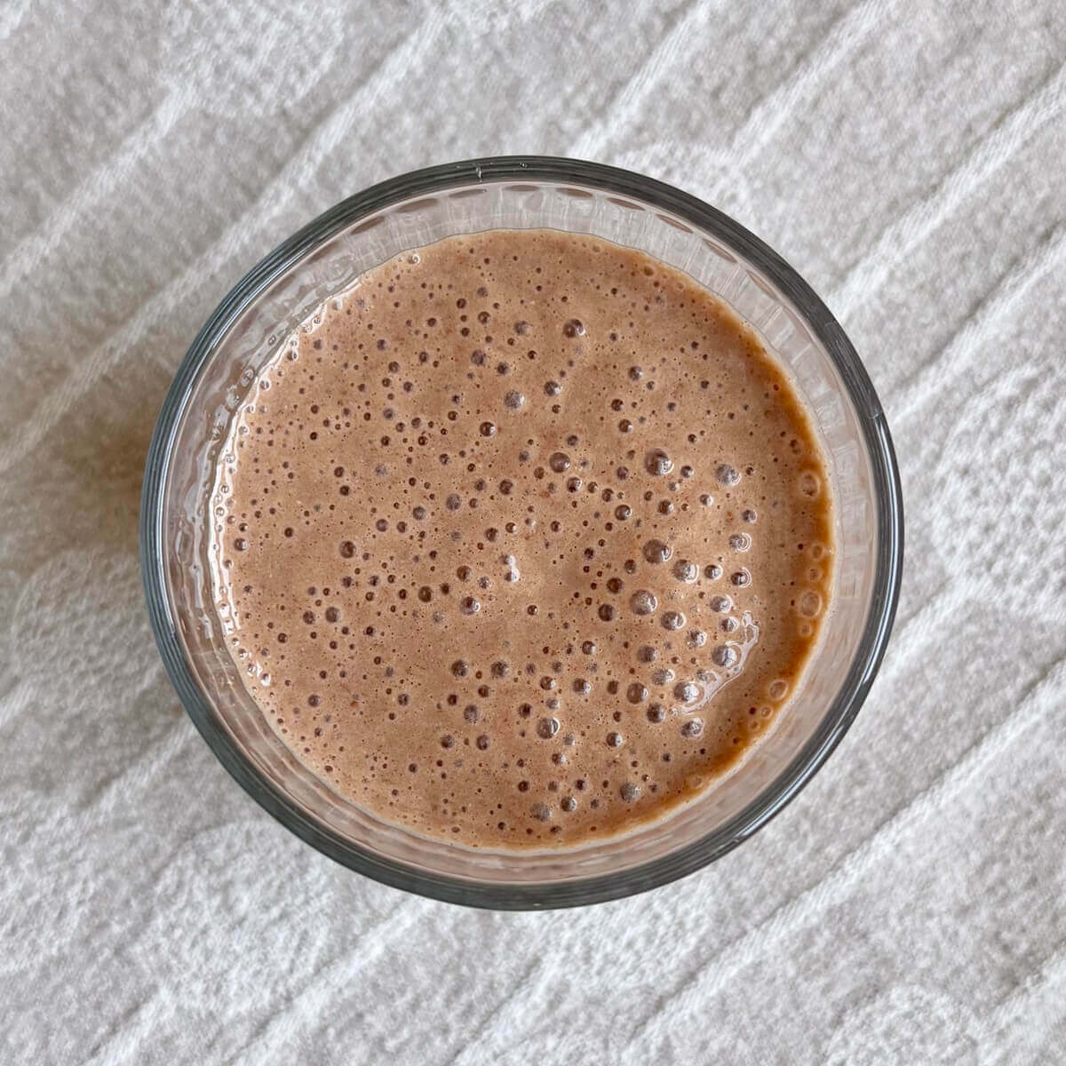 A flaxseed smoothie in a glass on a beige placemat.
