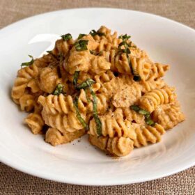 Rotini noodles smothered in lentil pasta sauce in a white bowl.