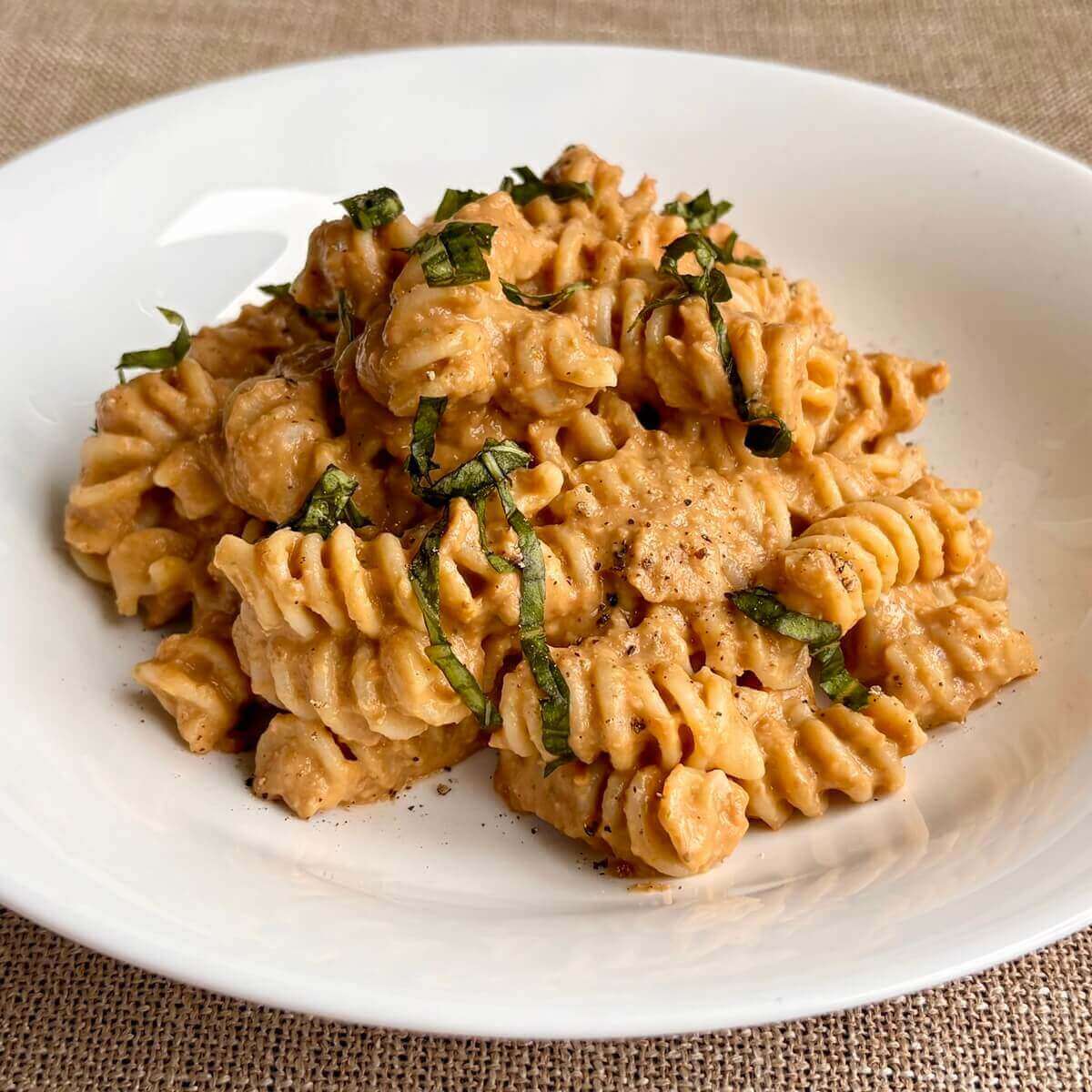 Rotini noodles smothered in lentil pasta sauce in a white bowl.