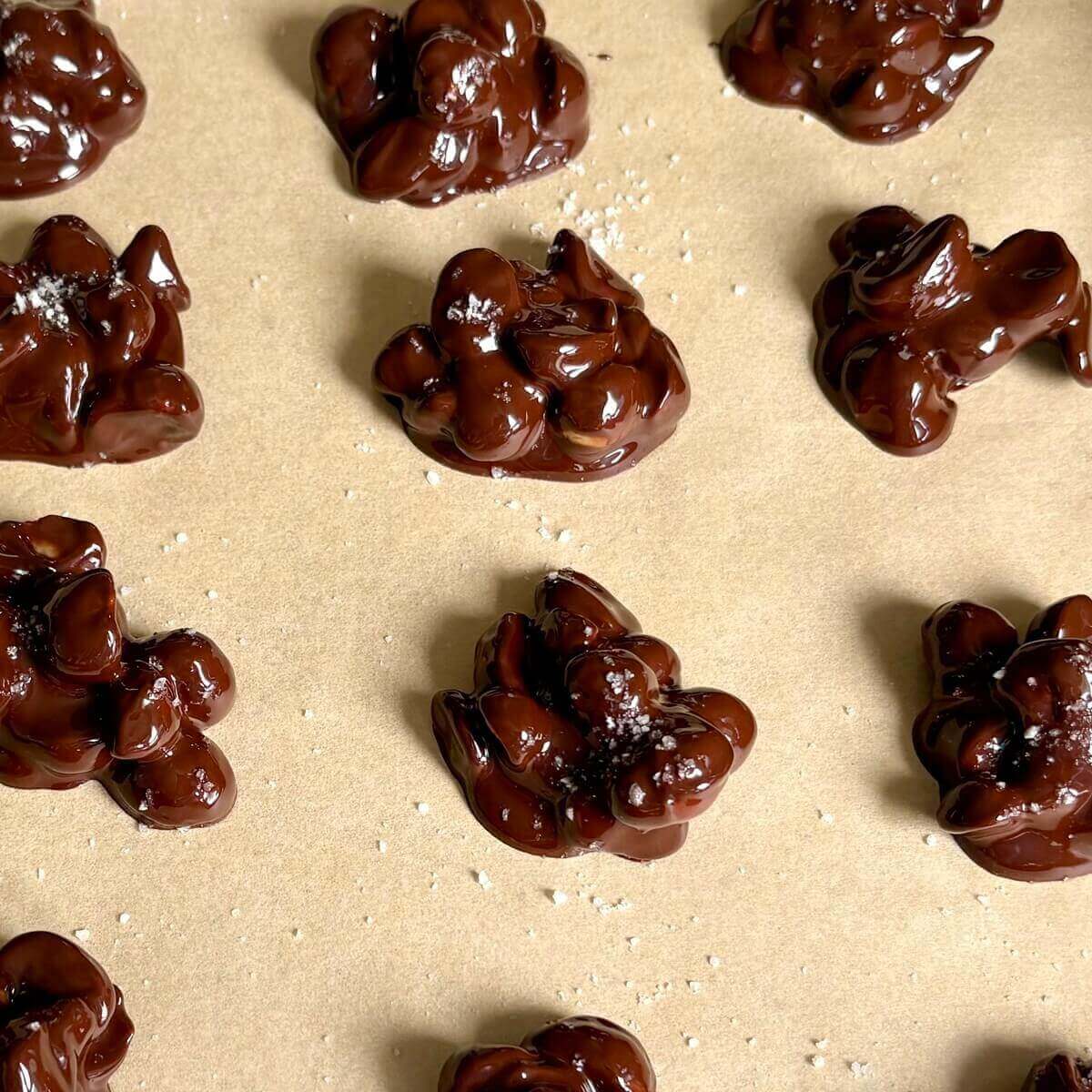 Chocolate macadamia clusters on a sheet pan lined with parchment paper.