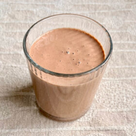 A macadamia smoothie in a glass on a beige placemat.