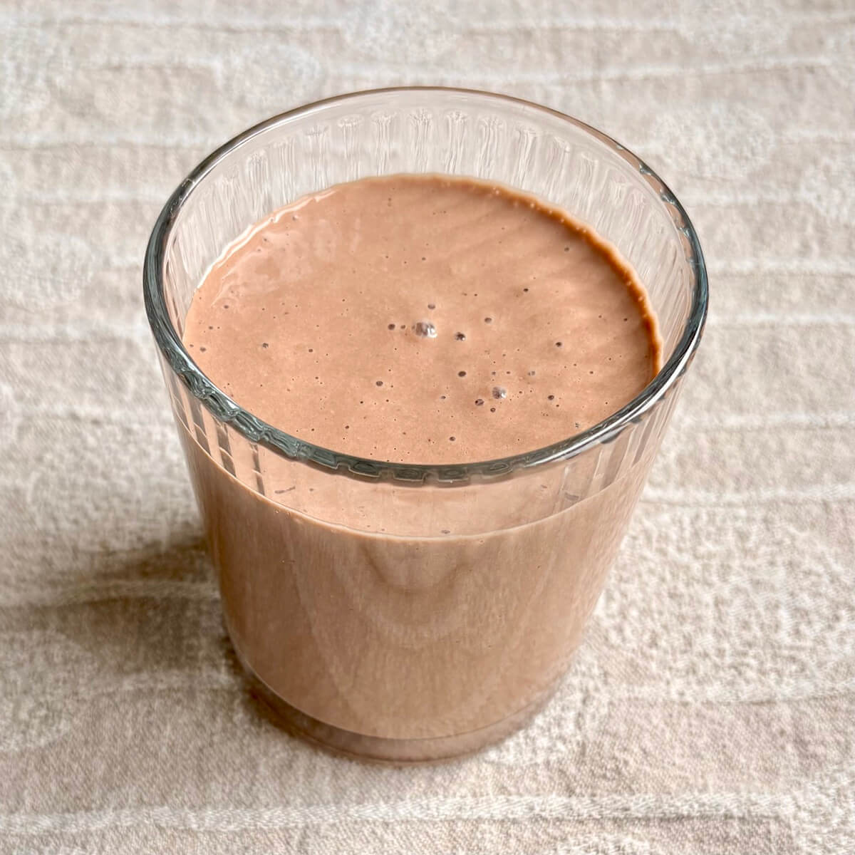 A macadamia smoothie in a glass on a beige placemat.