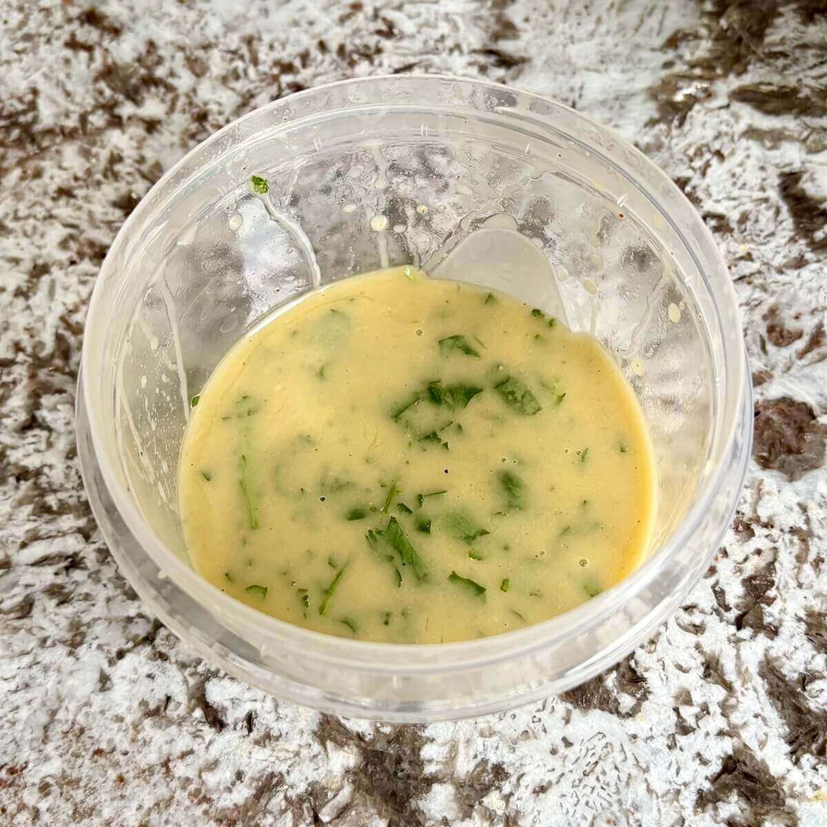 Vinaigrette made with parsley in a plastic container.