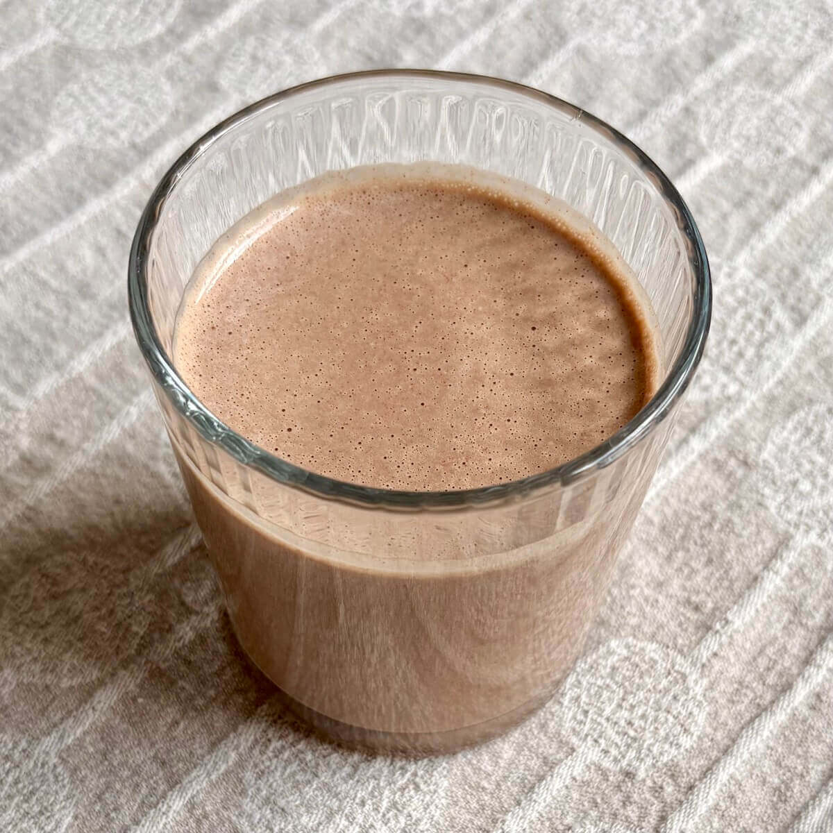 A peanut butter cup smoothie in a glass on a beige placemat.