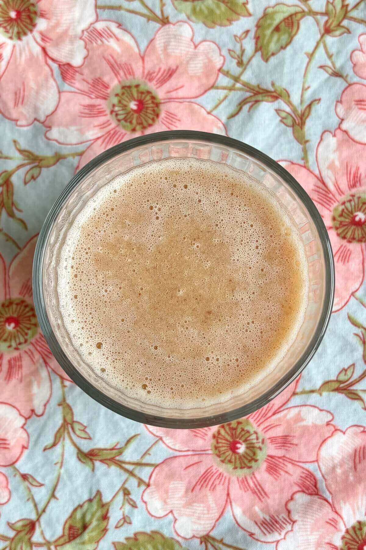 A lemon smoothie in a glass on a floral placemat.