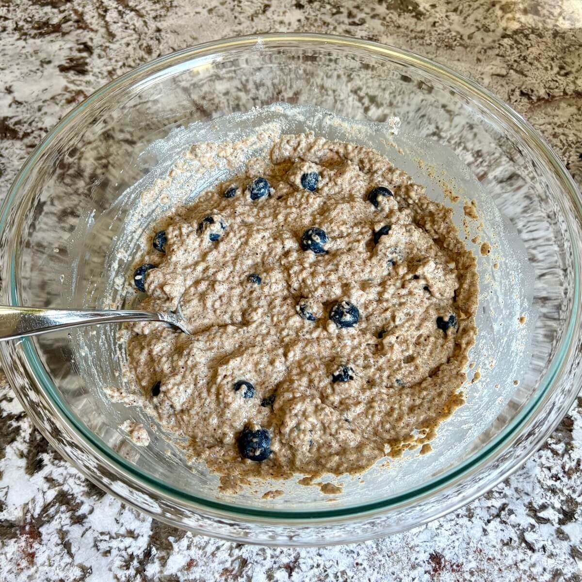 Chia muffin batter in a glass bowl with a spoon.