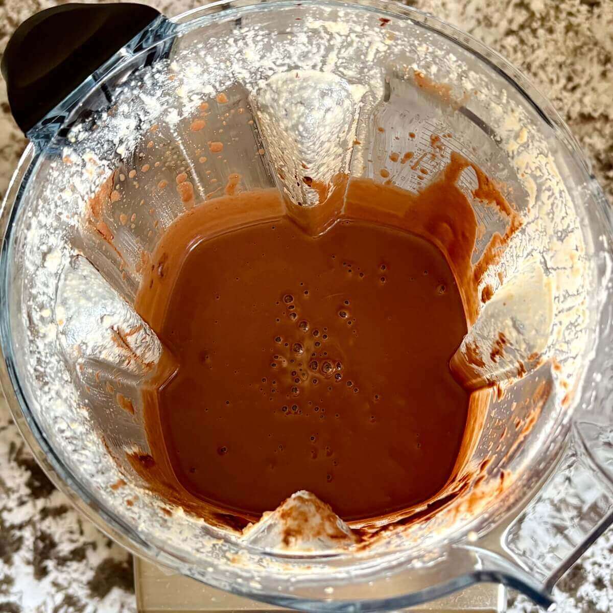 Melted chocolate, cashews, and other ingredients for mousse blended in a blender.