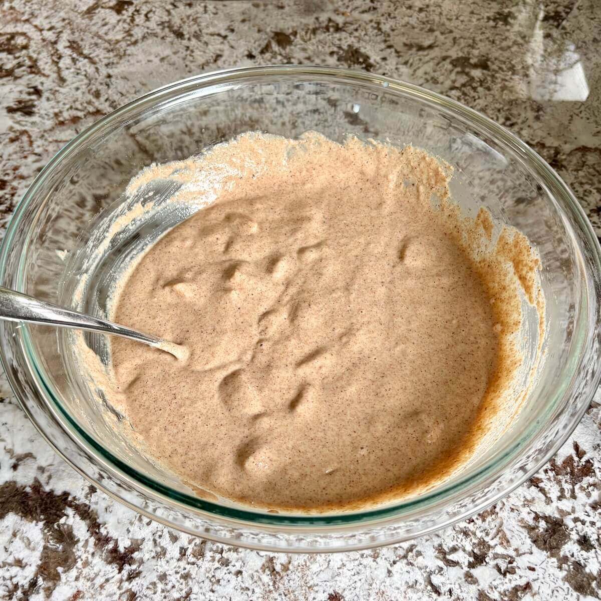Vegan pear muffin batter in a glass bowl with a spoon.
