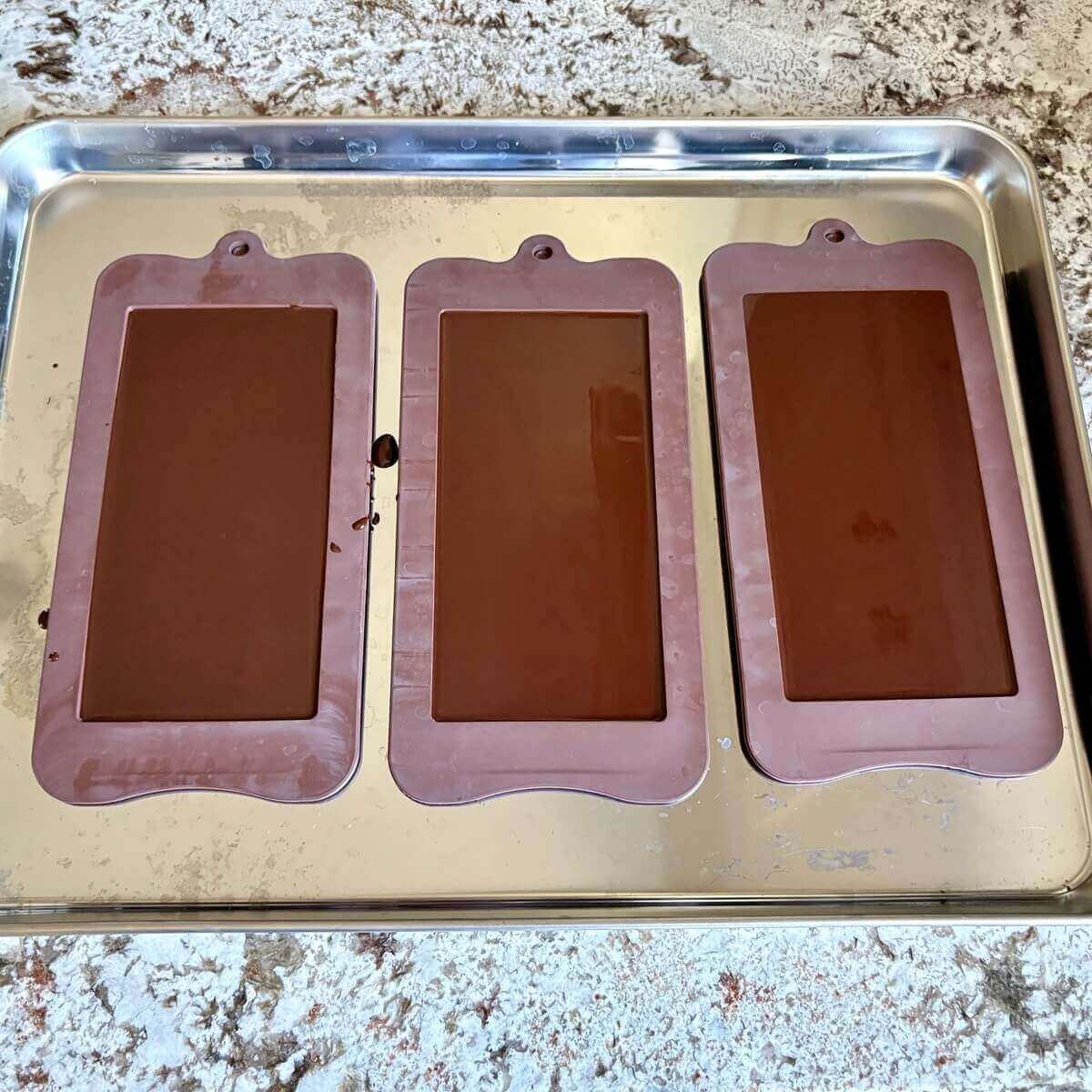 Three filled chocolate bar molds on a sheet pan.