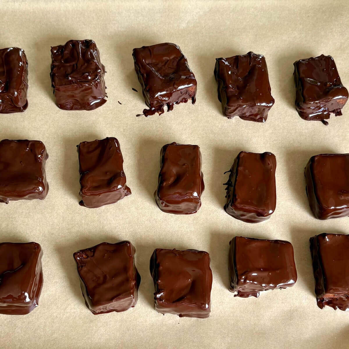 Dark chocolate dipped tofu pieces on a sheet pan lined with parchment paper.