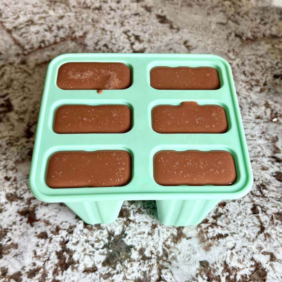 A popsicle mold filled with brown liquid.