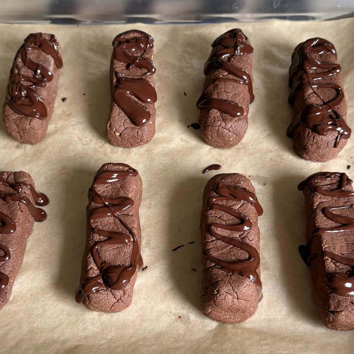 Low-carb chocolate-drizzled protein bars on a sheet pan lined with parchment paper.