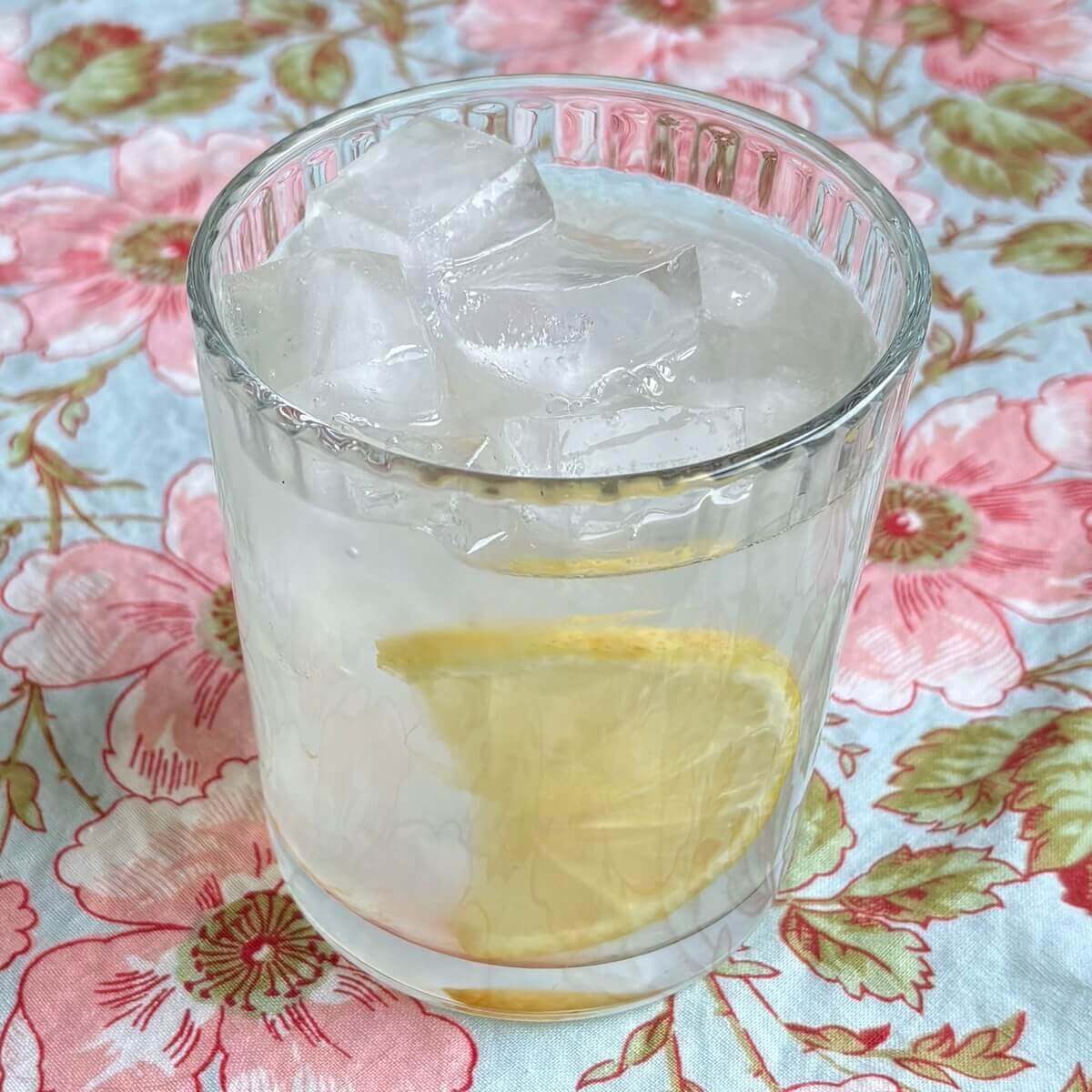 A glass of monk fruit lemonade with ice cubes and a lemon slice.