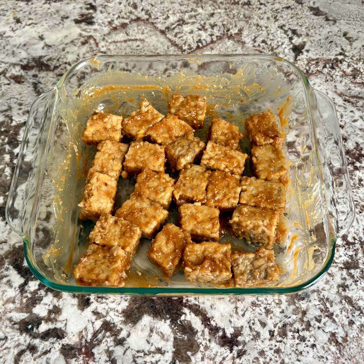 Tempeh in a sweet marinade in a glass baking dish.