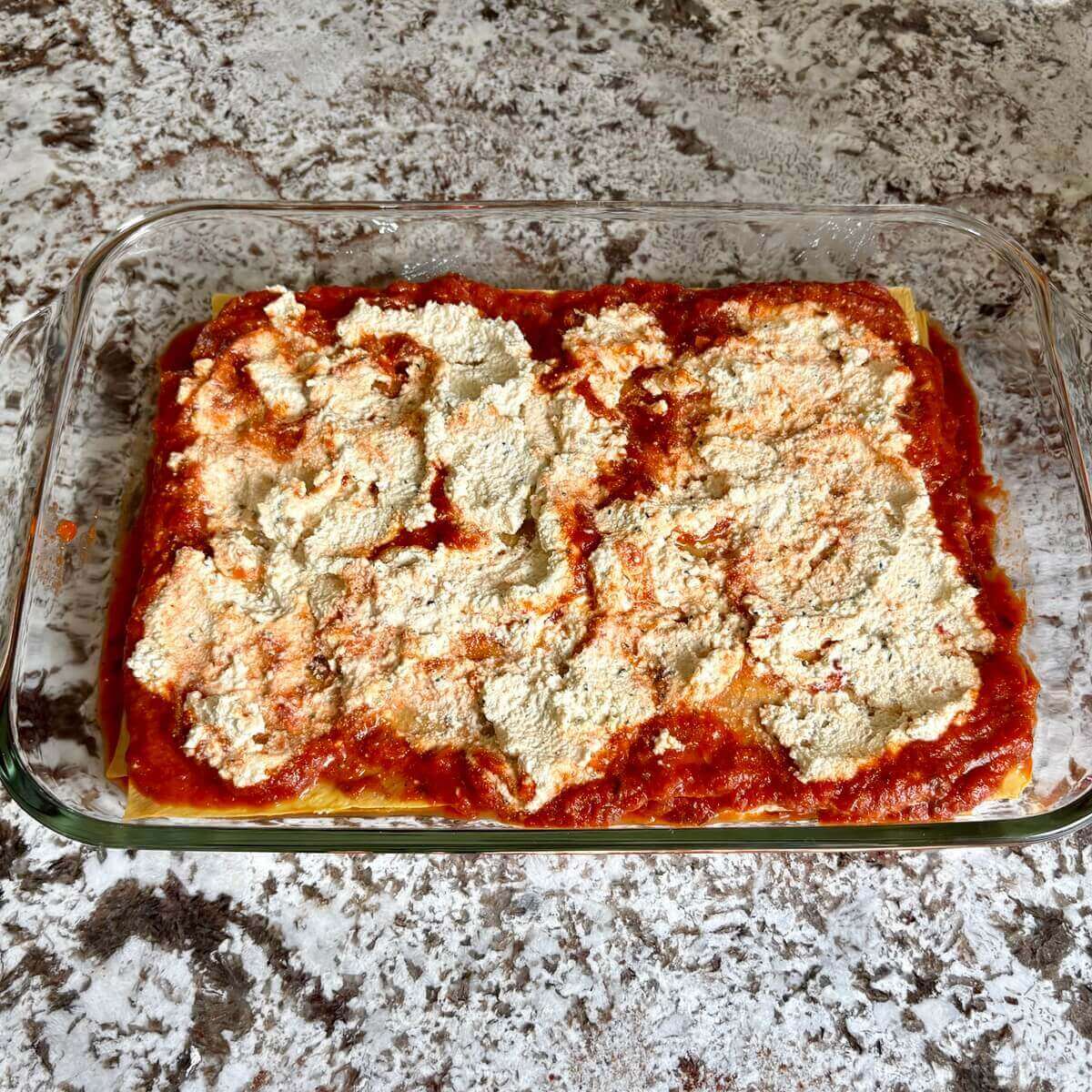 Unbaked vegan lasagna in a glass baking dish.