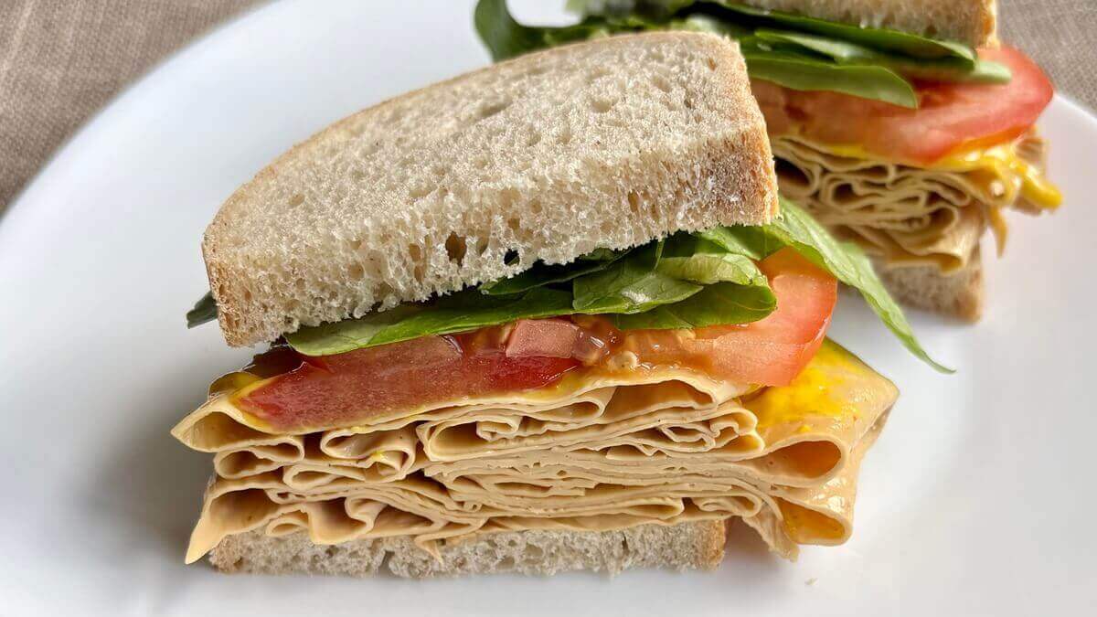 A sandwich with vegan deli turkey slices on a white plate.