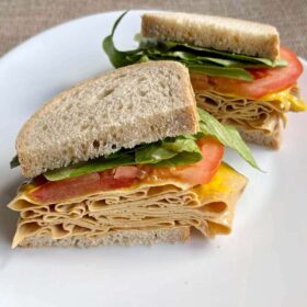 A sandwich filled with lettuce, tomato, and vegan turkey slices.
