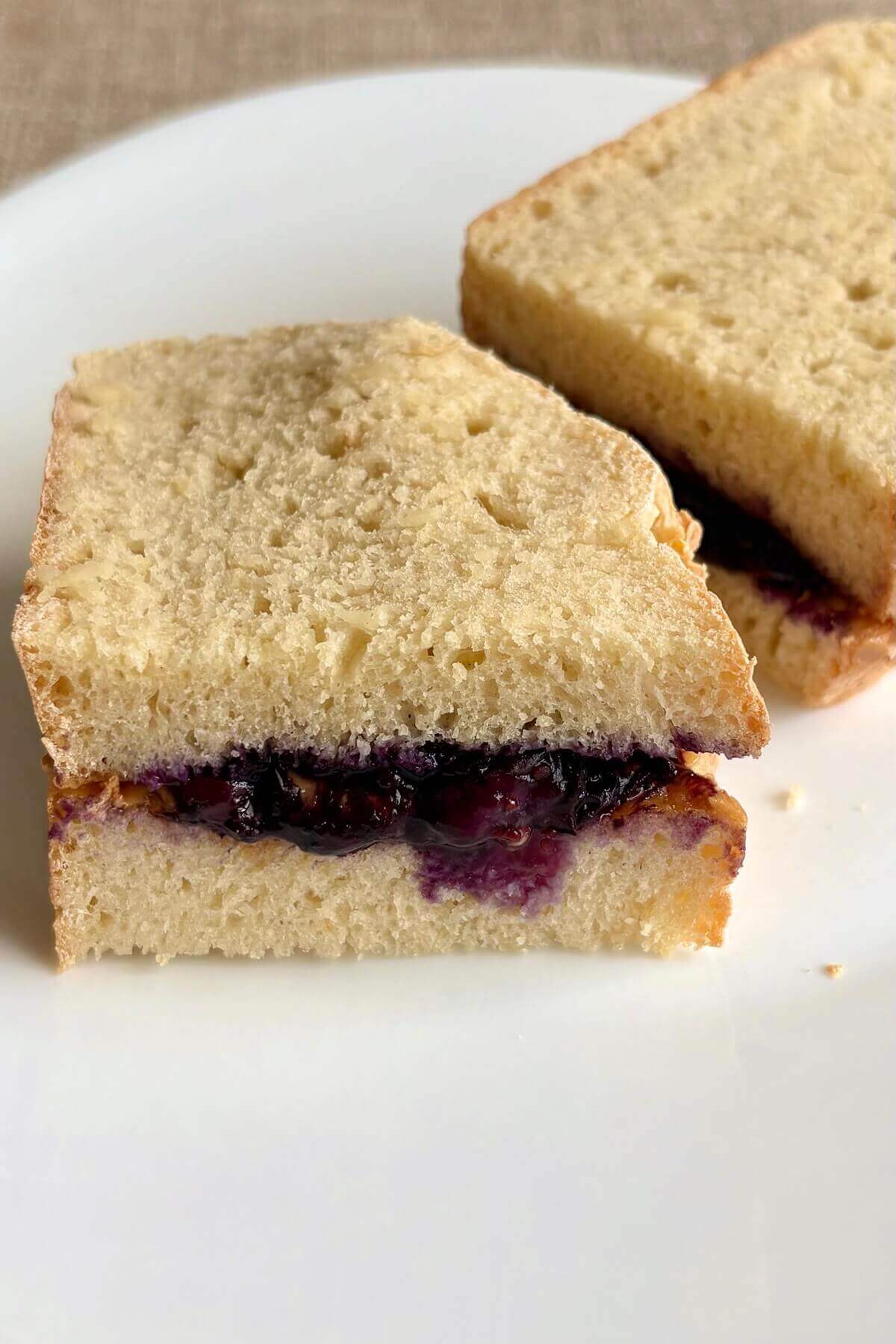 A peanut butter and blueberry jam sandwich on a white plate.