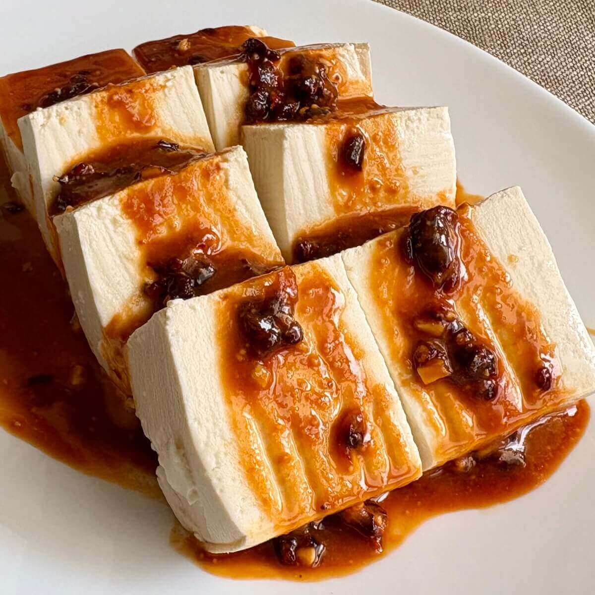 Slices of cold tofu drizzled with a red sauce.