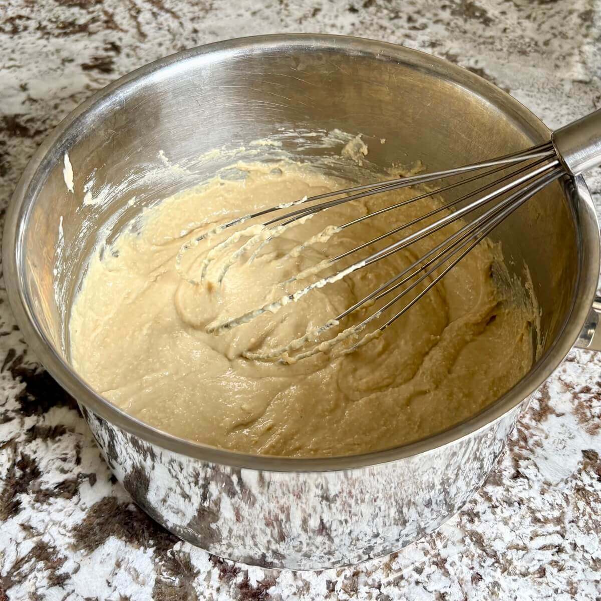 Gooey vegan cheese being whisked in a steel pot.