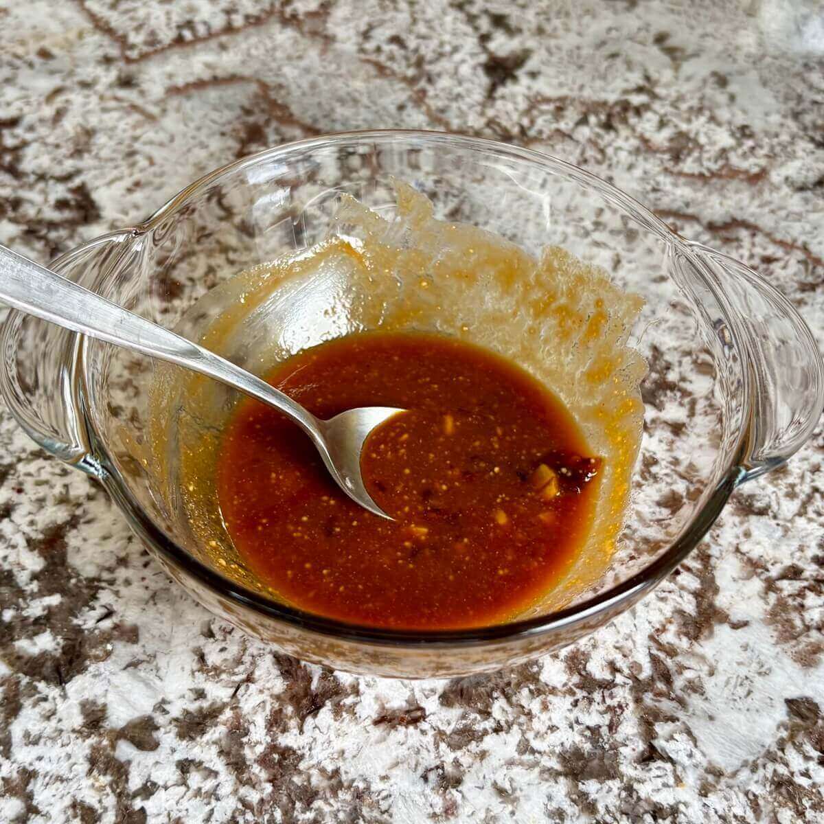 Sauce for tofu in a glass bowl with a spoon.